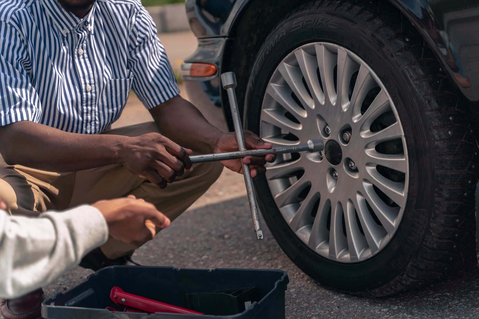 An adult showing a teenager how to change a car tire